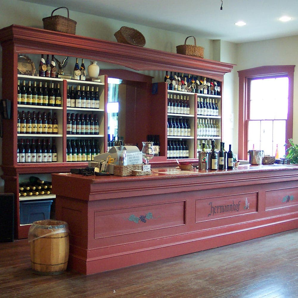 A wine tasting room featuring shelves filled with bottles of wine and a wooden bar with tasting accessories.