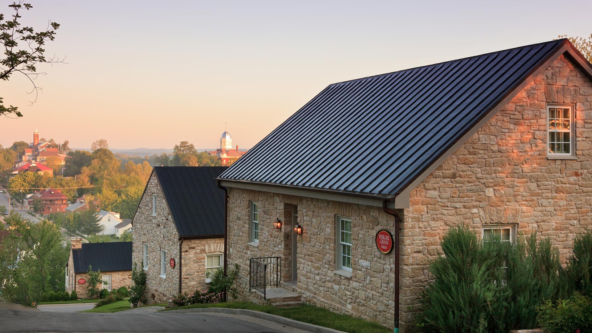 A stone house with a dark roof overlooks a quaint town at sunrise.