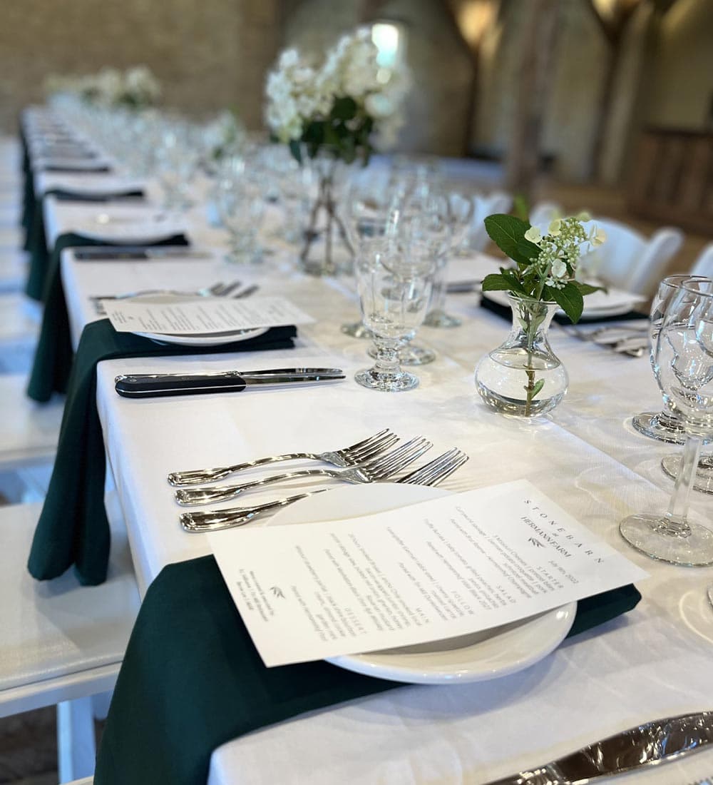 A beautifully set dining table with green napkins, menus, and flower arrangements in clear vases.