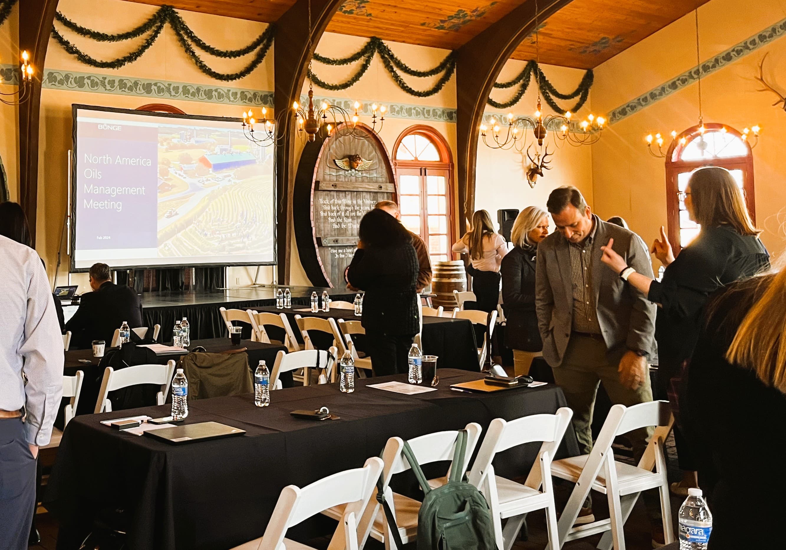 A group of professionals gathers in a conference room for a meeting, with a presentation screen displaying "North America Oil Management Meeting."