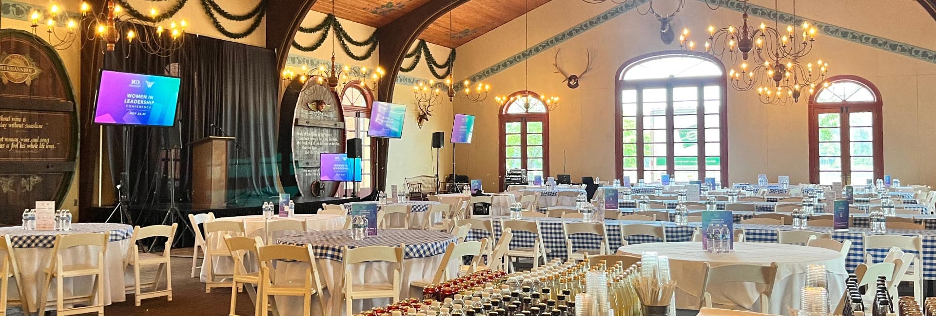 A decorated event space set up for the "Women in Leadership Conference" with tables, chairs, and a stage.