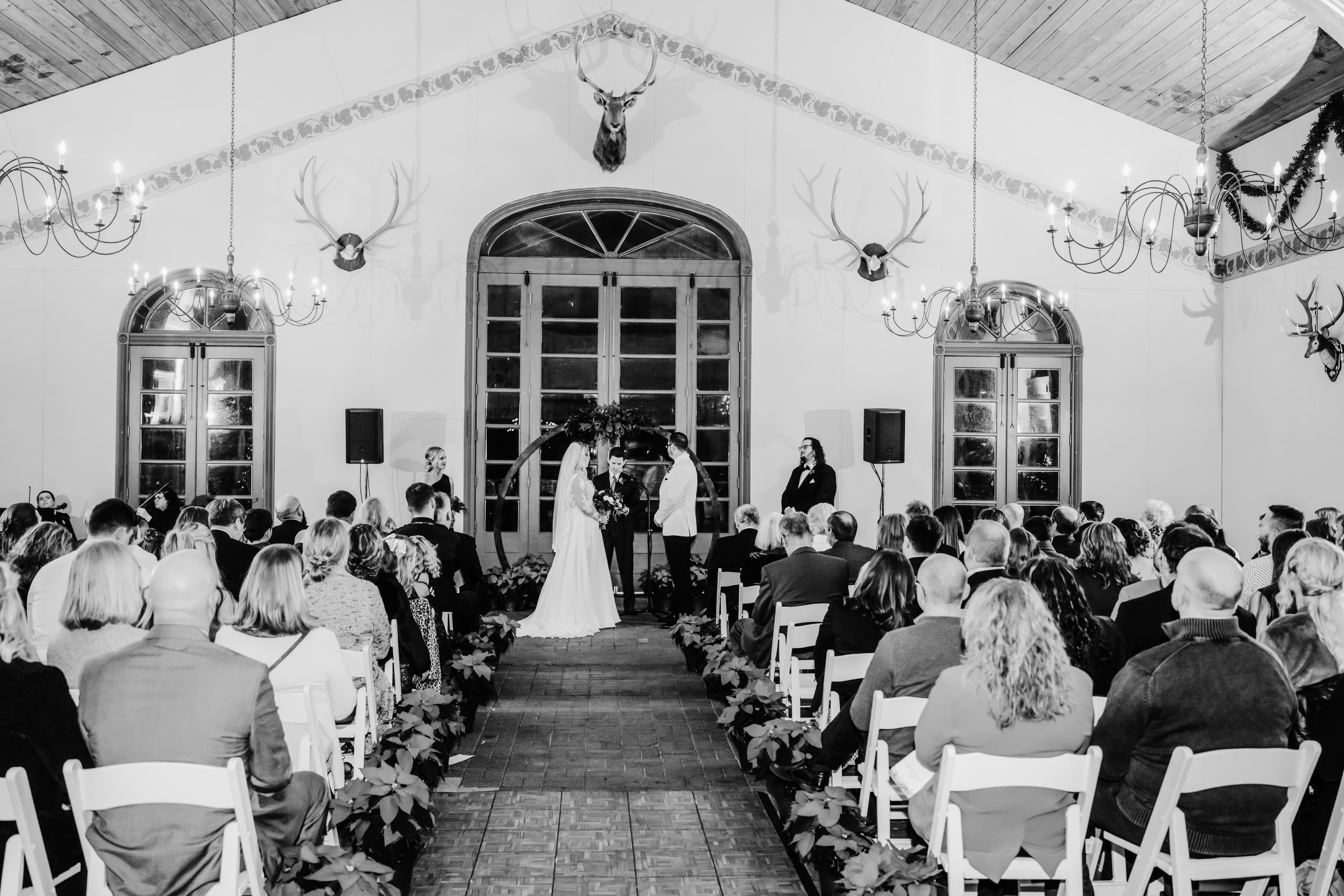 A wedding ceremony takes place indoors with a couple at the altar and guests seated around them.