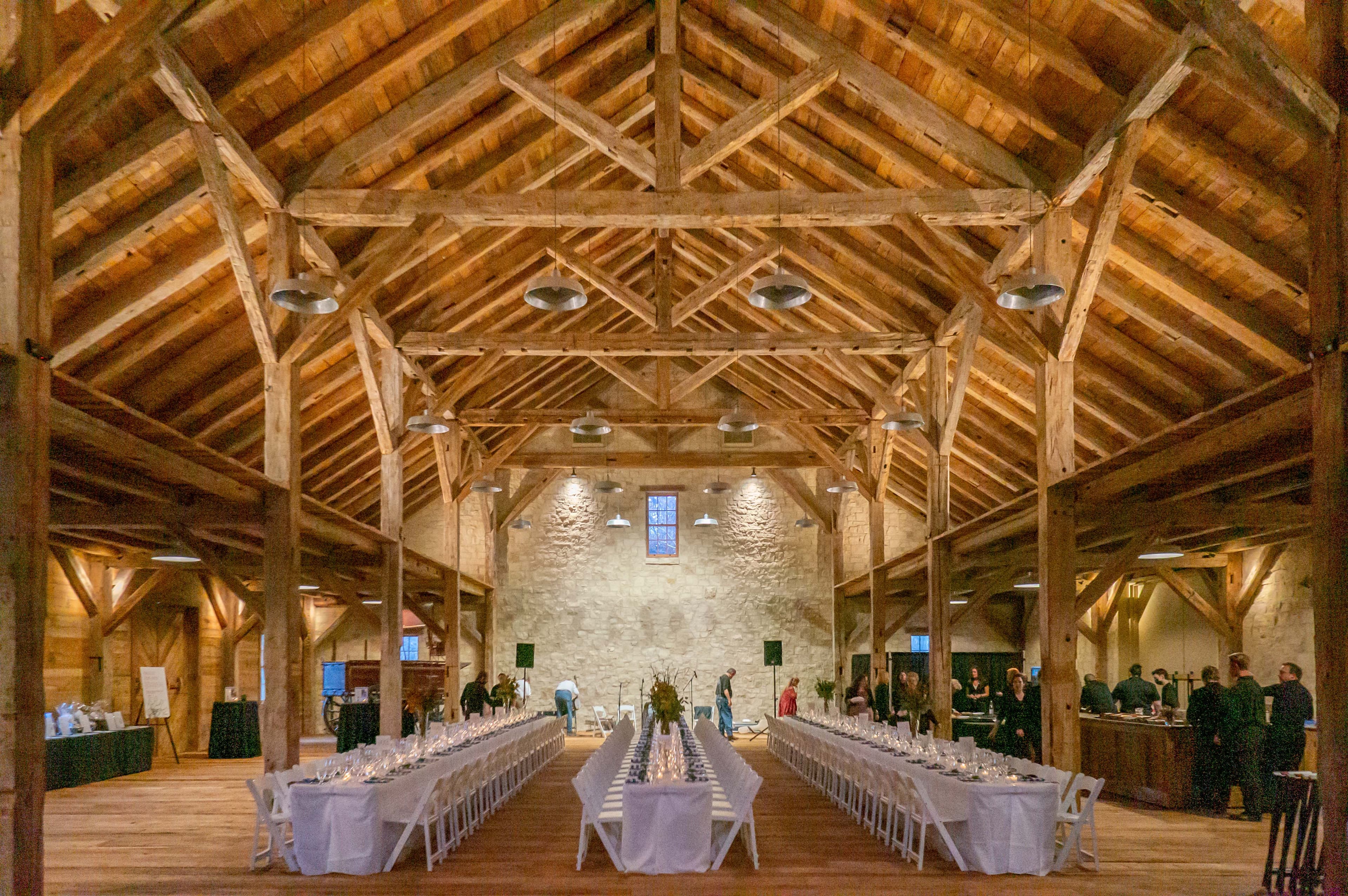 A spacious, rustic event space with wooden beams and long dining tables set up for a gathering.