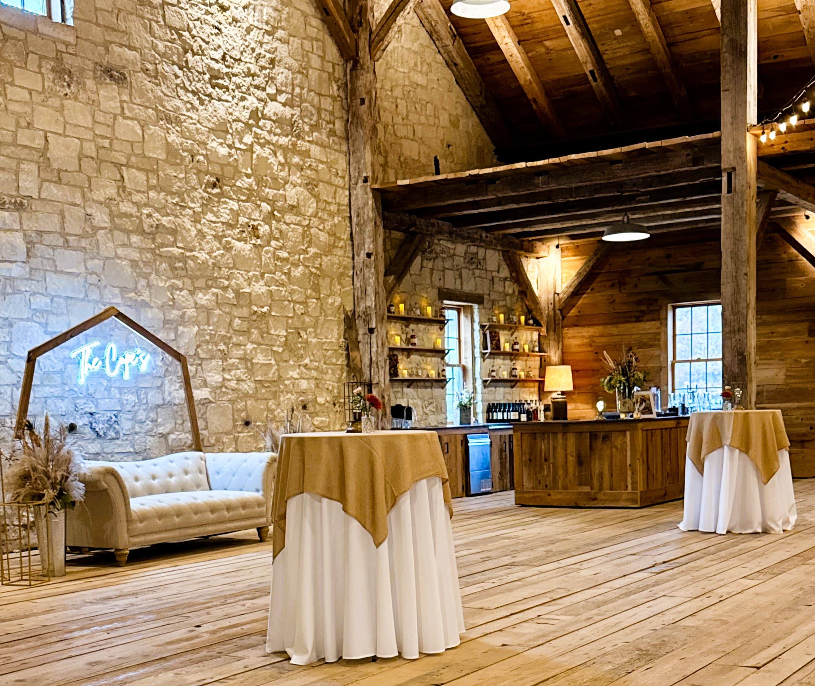 A rustic event space featuring wooden beams, stone walls, and elegantly set tables.