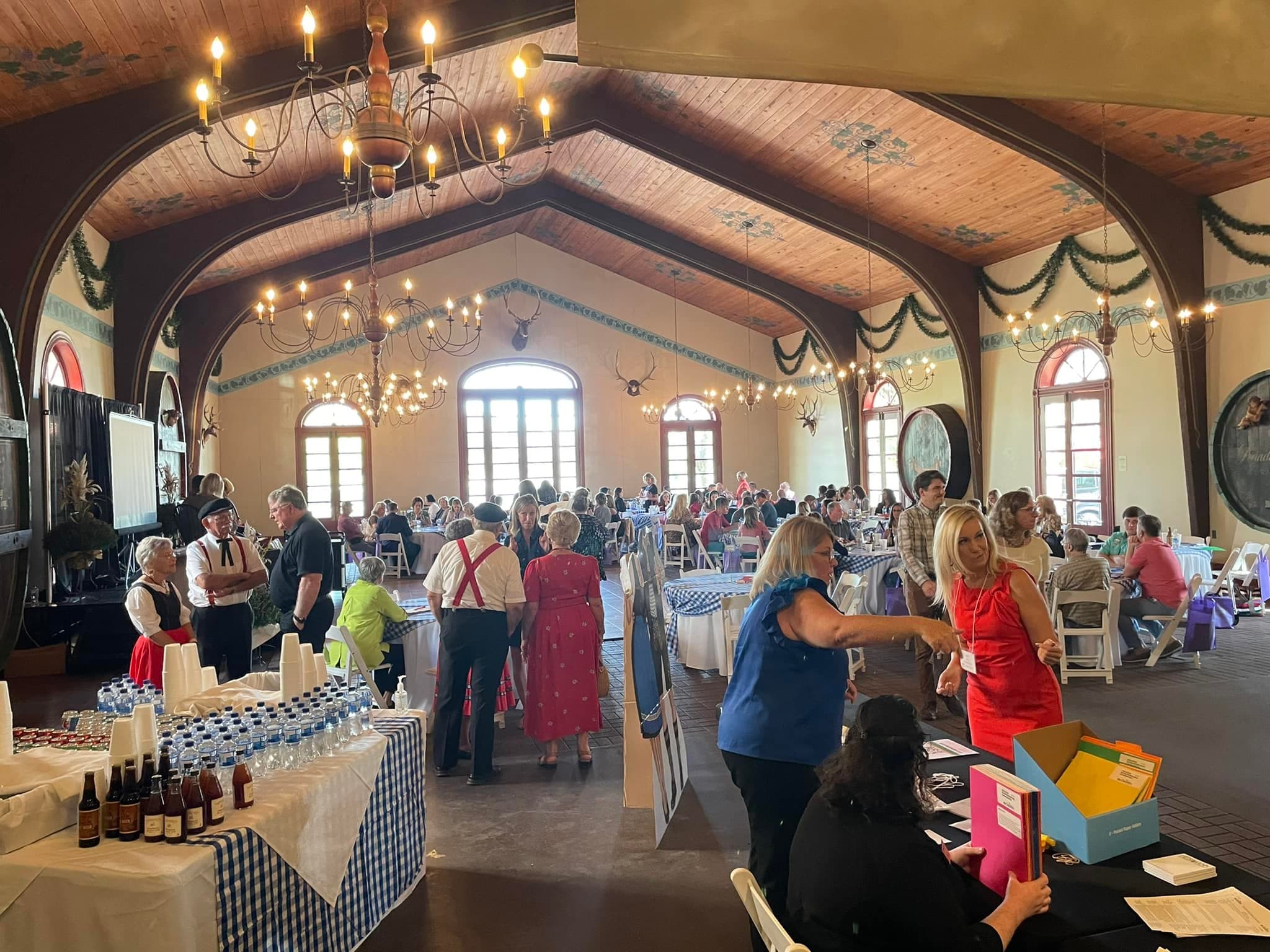 A lively gathering with many people seated at tables in a decorated hall, engaged in conversations and activities.