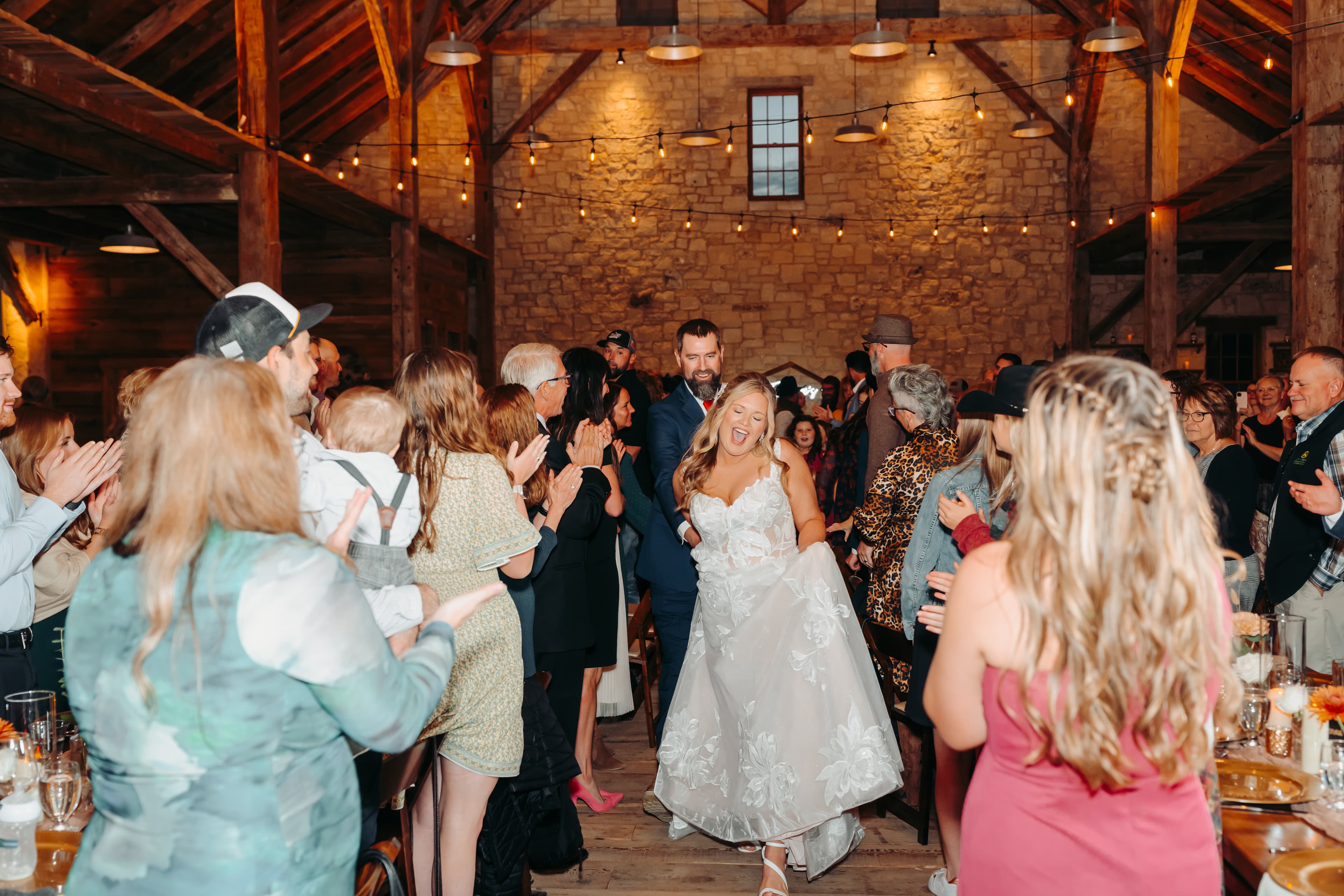 A joyful bride walks through a cheering crowd in a rustic venue.