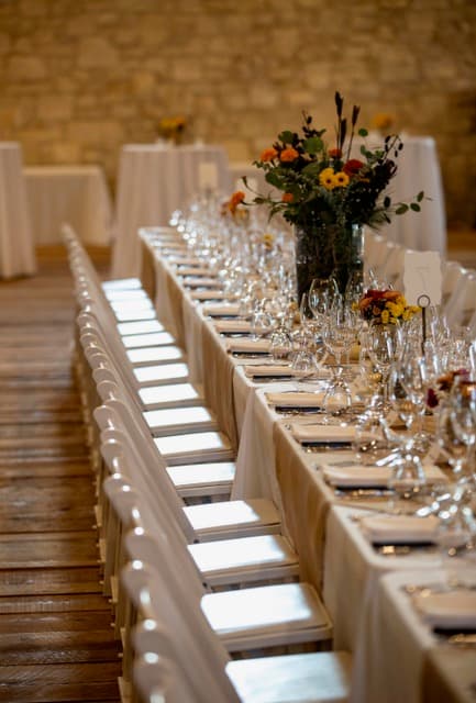 A long banquet table elegantly set with glassware and a vibrant floral centerpiece in a rustic venue.
