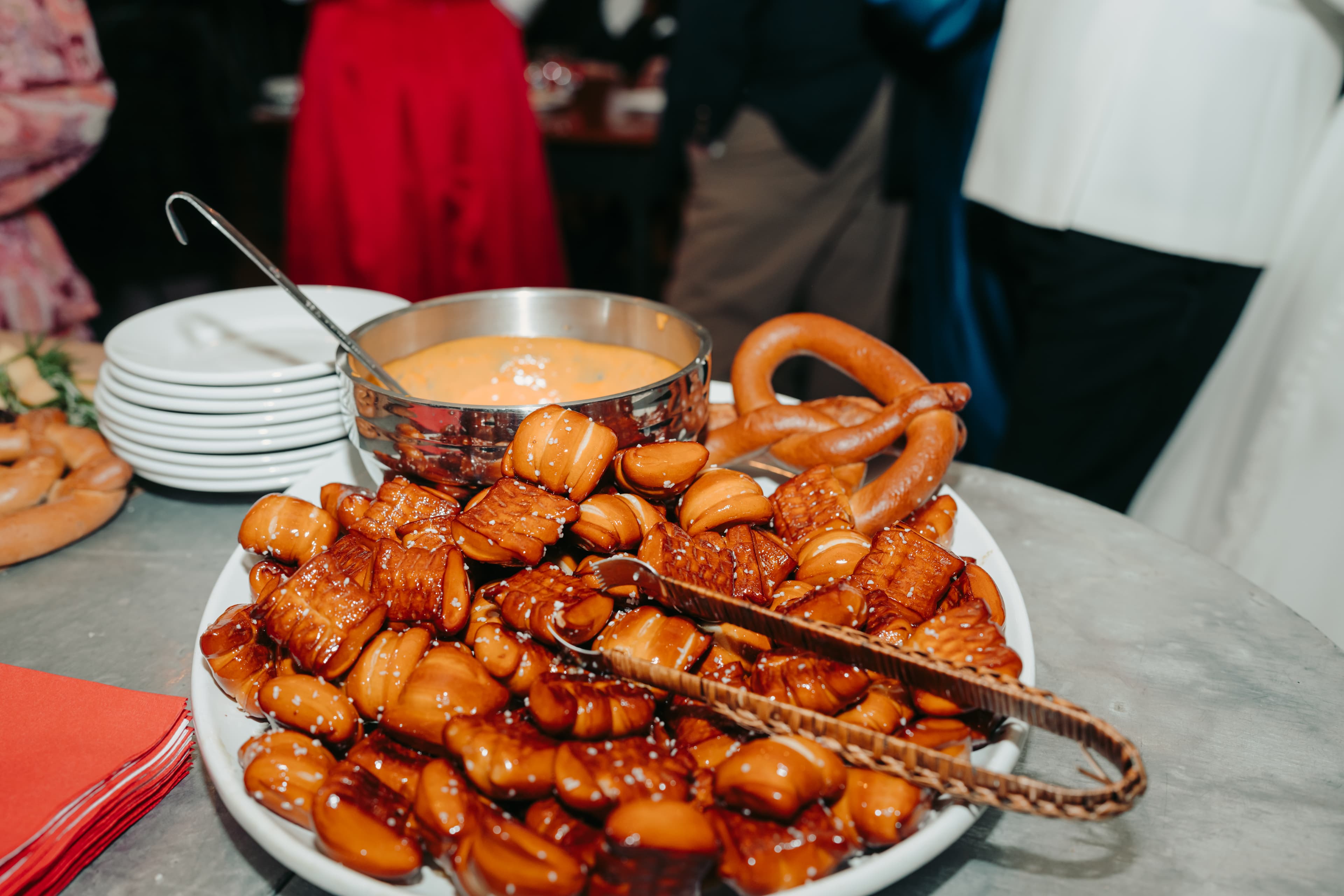 A plate of glazed pastries and a bowl of dipping sauce, with pretzels beside them.